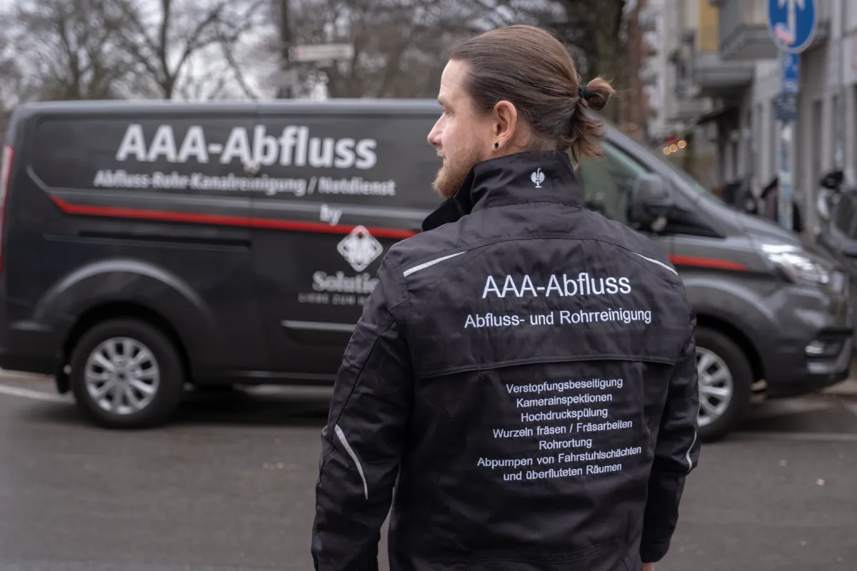 AAA-Abfluss Arbeitskleidung mit Leistungsübersicht vor dem Firmenfahrzeug